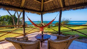 An outdoor seating area with wicker chairs and a table, overlooking a beach. - Amani Beach Resort  (Kutani)