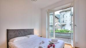 A hotel room with a bed, white linens, a neatly made bed with towels and flowers, and a view of a building through a glass door. - Bellinzona in Centro (Bellinzona)
