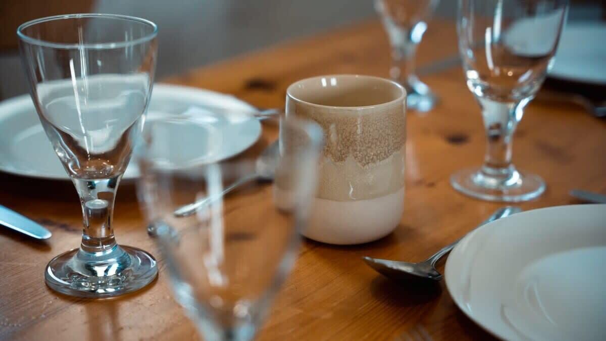 Une table en bois, agrémentée de verres transparents et d’une tasse en céramique, évoquant un décor de salle à manger.