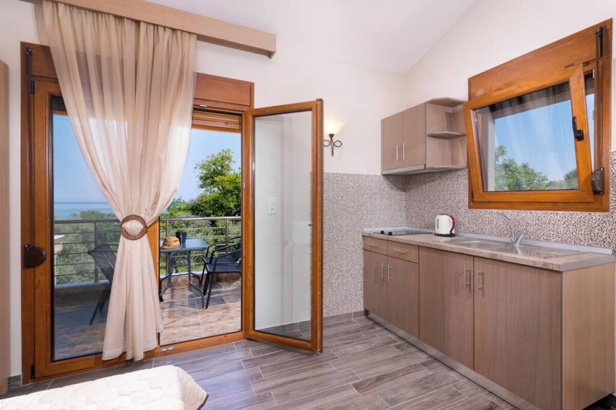 A modern kitchen with a large window, a sliding glass door leading to a balcony, and a small dining area.