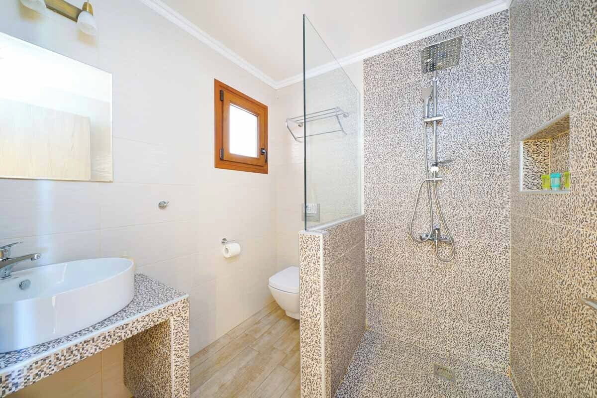 Un baño con lavamanos blanco, cabina de ducha de vidrio y un inodoro.