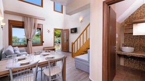 A spacious living area with a dining table, chairs, a sofa, a staircase, and a view of the outdoors. - Kapsogeorgis Rooms (Thasos)