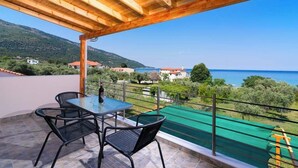 A covered outdoor area with a table and chairs, overlooking a scenic landscape with a view of the sea and hills. - Kapsogeorgis Rooms (Thasos)