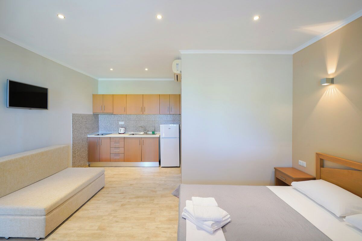 Habitación de hotel compacta con kitchenette, sofá, cama y mesita de noche.