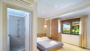 A bedroom with a bed, a wooden wardrobe, a window with a view, and a shower area. - Kapsogeorgis Rooms (Thasos)