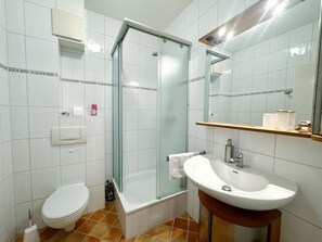 Une salle de bain comprenant des toilettes, une douche à parois de verre, un lavabo et un miroir.