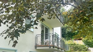 Ein zweistöckiges Gebäude mit einem Balkon, einem Fenster mit Rollläden und einem Weg, der zu einem Tor führt.