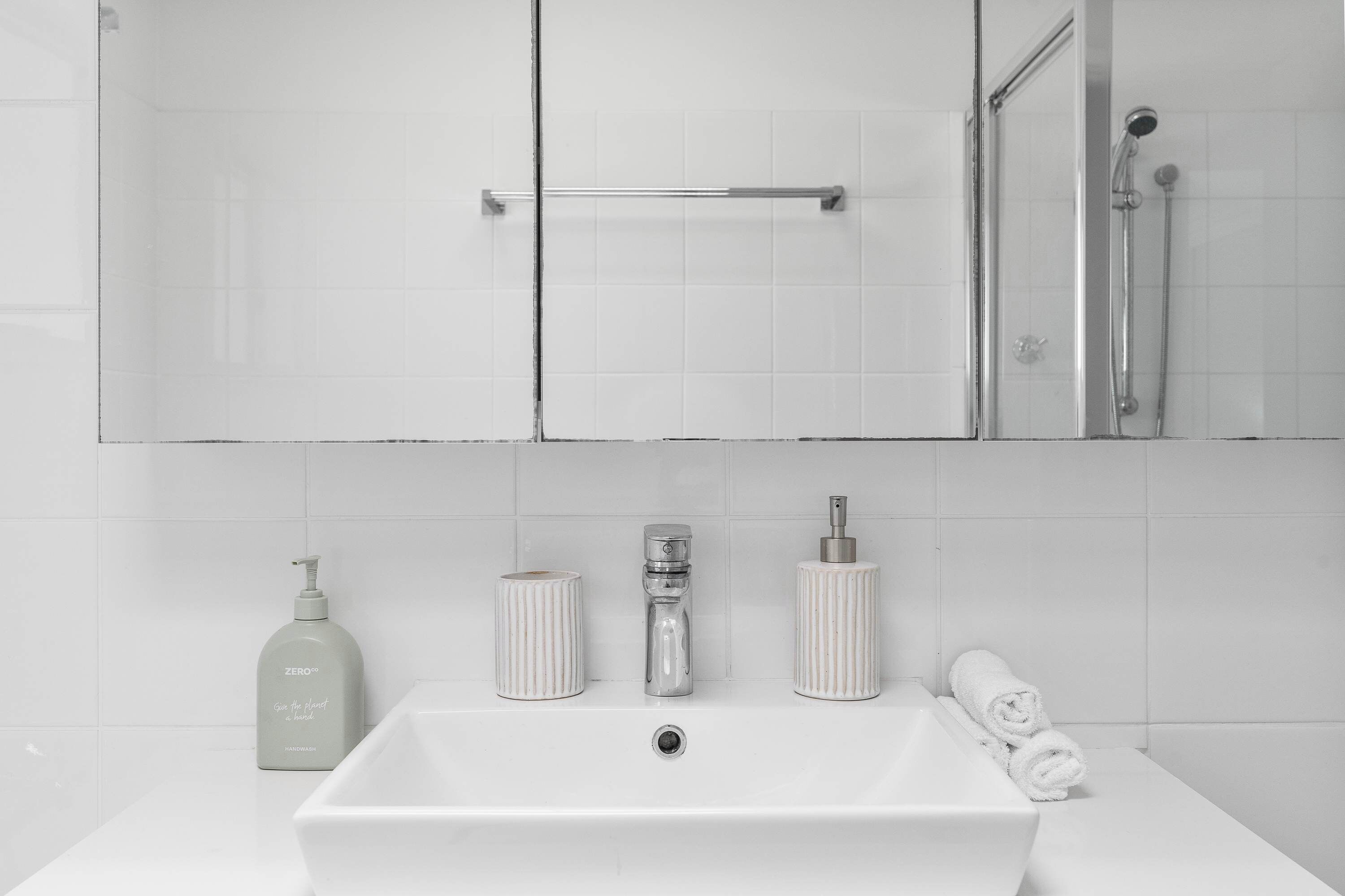 A bathroom with a white sink, a mirror, and a shower.