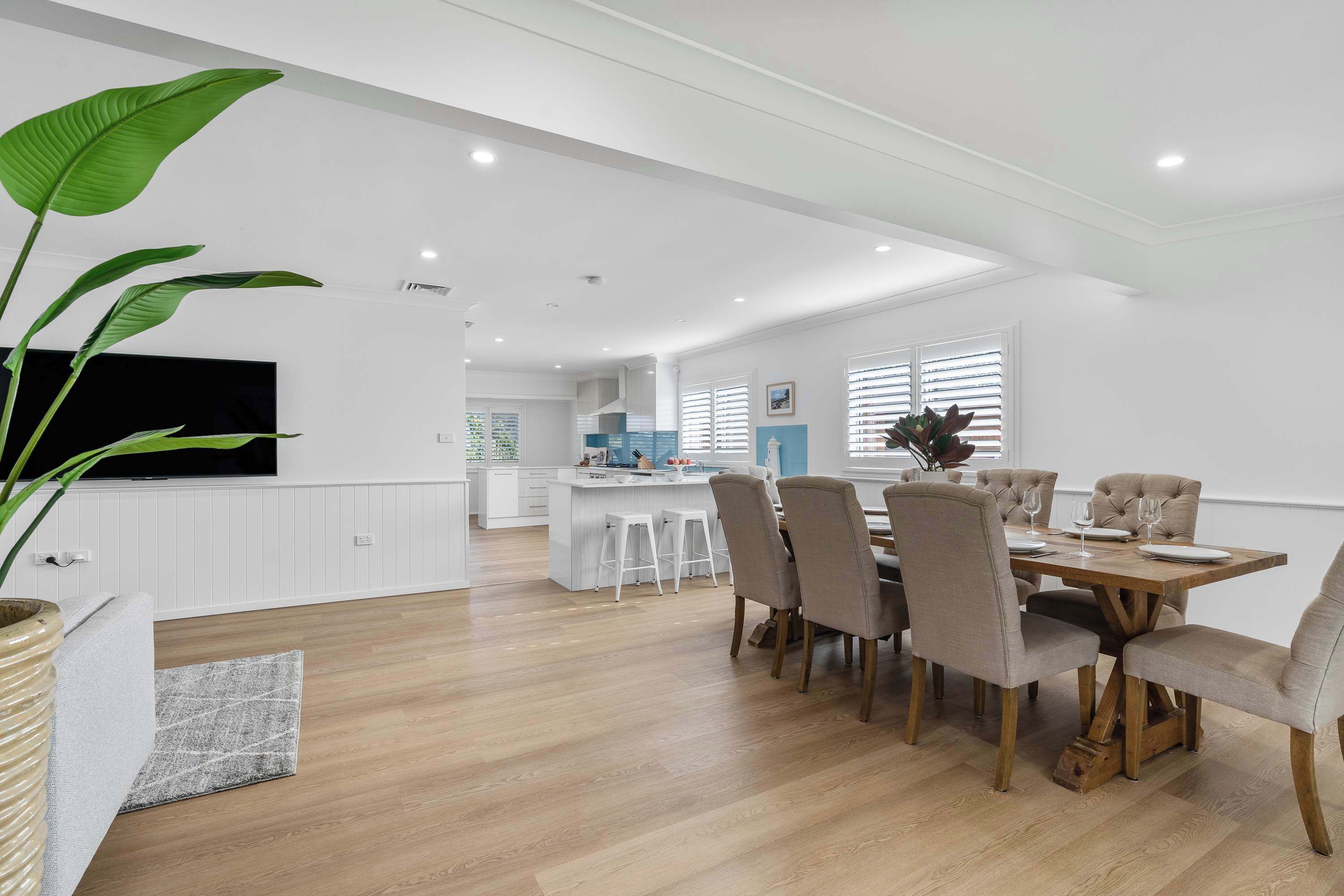A modern kitchen with white cabinetry, a central island, and a dining area with a wooden table and chairs.