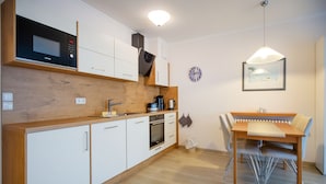 A modern kitchen with white cabinets, a built-in microwave, a stove, and a dining area with a wooden table and chairs.