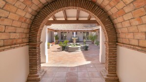An arched brick entrance leading to a courtyard with a tiled roof, potted plants, and a central fountain. - Cortijo Villa Padierna El Lago (Benahavis)