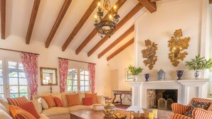 A cozy living room with a fireplace, wooden beams, and striped cushions. - Cortijo Villa Padierna El Lago (Benahavis)