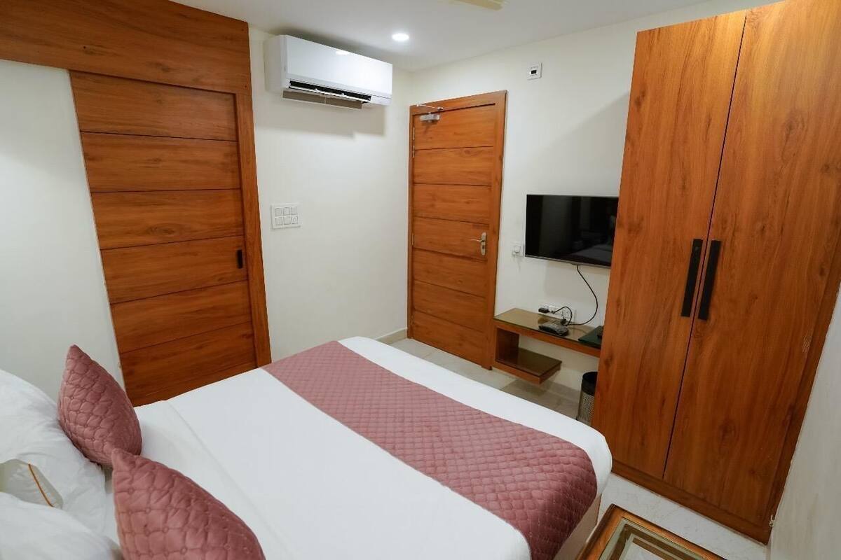 A bedroom with a bed, wooden wardrobe, a TV, and an air conditioning unit.