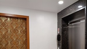 Een moderne lift met een metalen afwerking, een aan de muur bevestigd telefoon en een decoratieve deur met geometrische patronen.