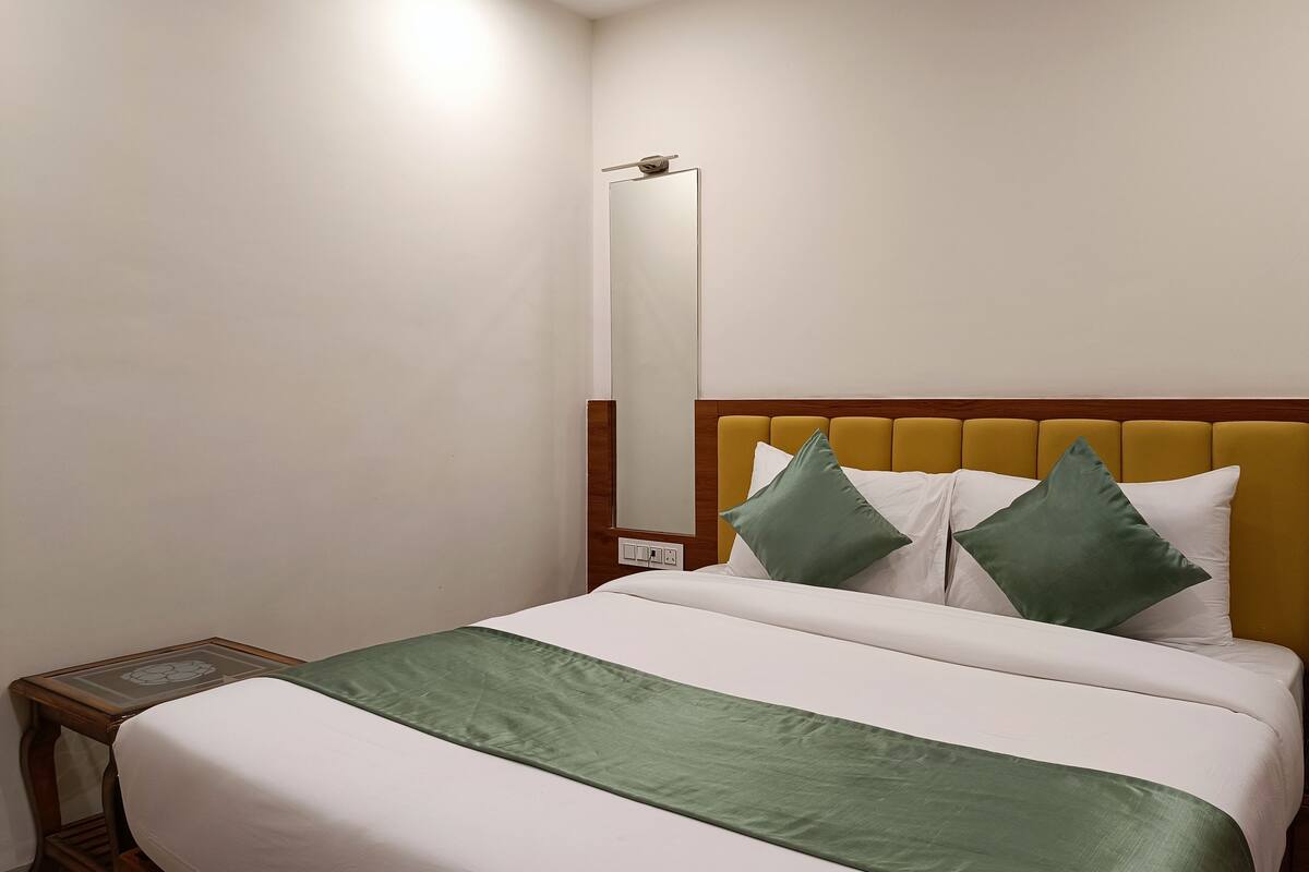 A hotel room with a bed, a nightstand, a mirror, and a wooden headboard.