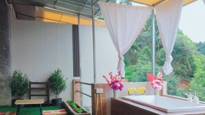 A room with a green artificial turf floor, a wooden bench, a small table with a vase of flowers, a wooden cabinet, and a window with a view of greenery. - Mon Nao  (Mae Rim)
