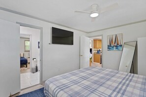 Ein Schlafzimmer mit Bett, Deckenventilator, einem Gemälde und Blick zur Küche.