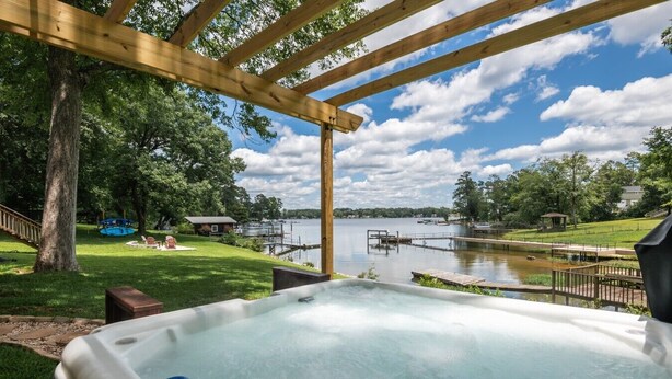 A hot tub under a wooden pergola with a lake view.