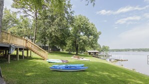 A lakeside property with a wooden deck, kayaks, and a dock.