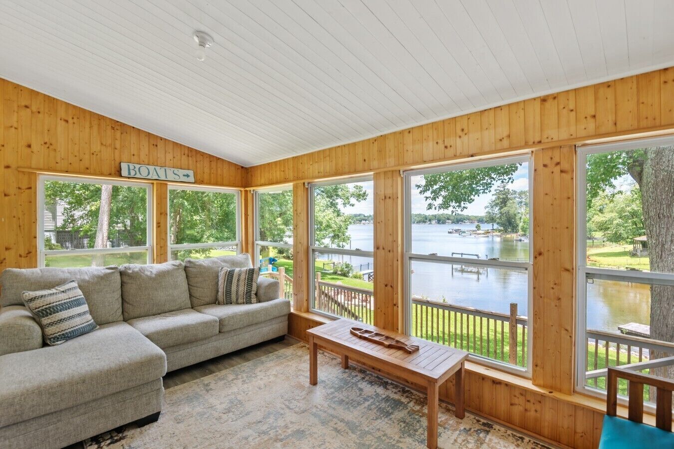 Une cabane dotée d’une grande fenêtre donnant sur un lac, d’un canapé et d’une table en bois.