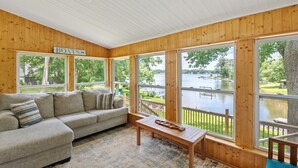 A cabin with a large window overlooking a lake, a sofa, and a wooden table.