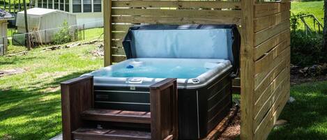 Un jacuzzi bajo una pérgola de madera en un patio trasero con césped y una valla al fondo.