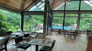 A spacious indoor area with wooden flooring and large windows offering views of lush greenery and a pool. - DOI LUANG SCENE (Chiang Dao)