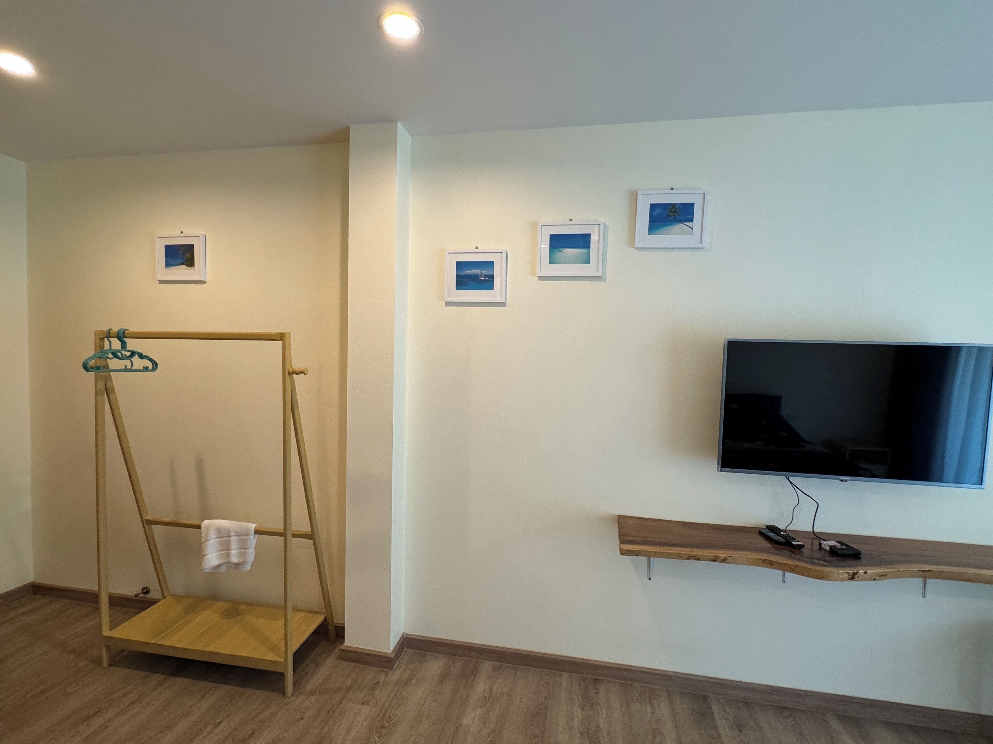 A room with a wooden swing chair, a television on a wooden shelf, and four framed pictures on the wall.