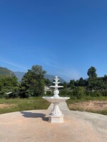 A white outdoor fountain with a tiered design, set on a paved area with a clear blue sky and mountains in the background.