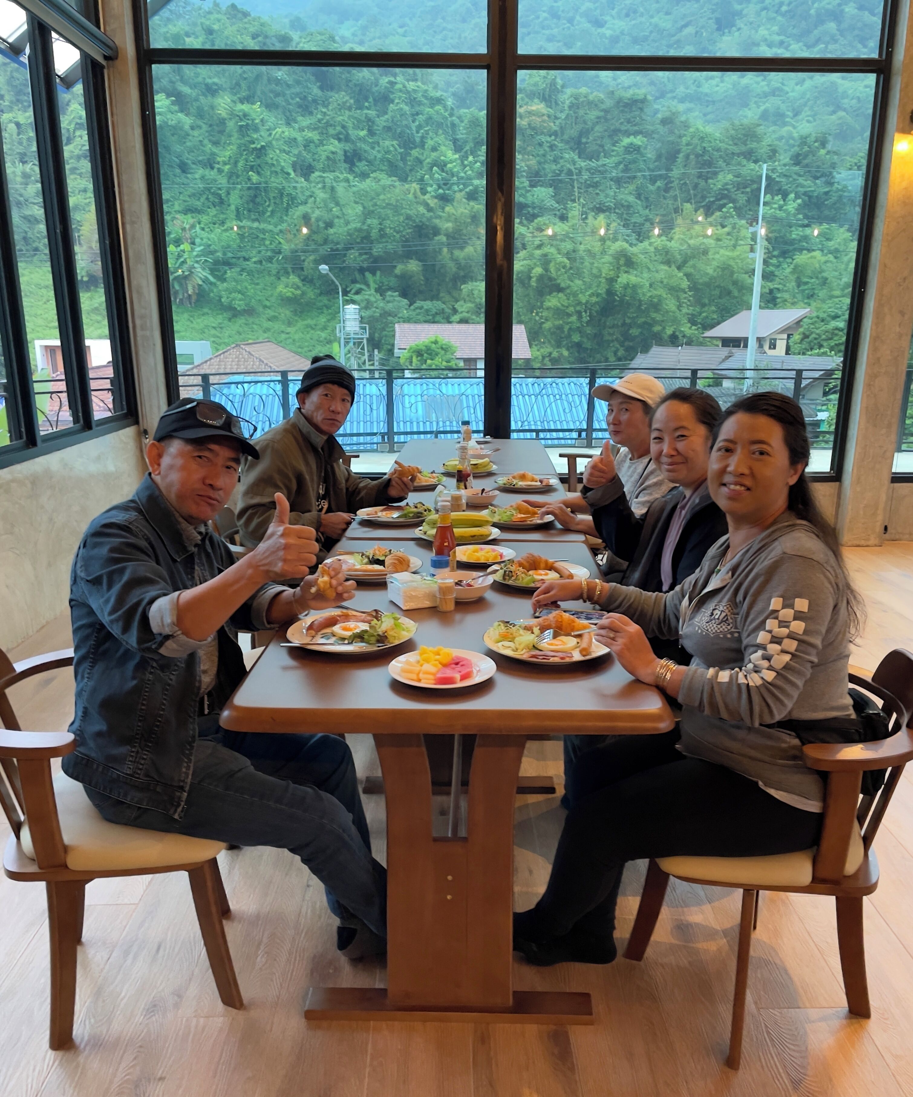 A group of people dining at a table with a view of a lush green landscape through large windows.