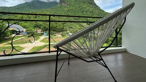 A hammock chair on a balcony with a view of a lush green mountain and a small building in the distance. - DOI LUANG SCENE (Chiang Dao)
