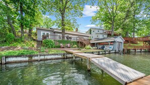 Una propiedad frente al lago con muelle, terraza de madera y una casa con balcón con vistas al agua.