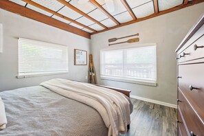 A bedroom with a large bed, two windows with blinds, a wooden ceiling, and a dresser. - The Lake Effect House (Dublin)