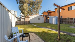 A backyard with a white chair, a small table, and a wooden fence. - Lake Court in the heart of Forster (Forster)