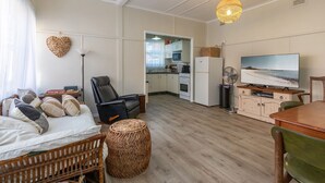 A cozy living room with a sofa, a chair, a TV, and a kitchen in the background. - Lake Court in the heart of Forster (Forster)