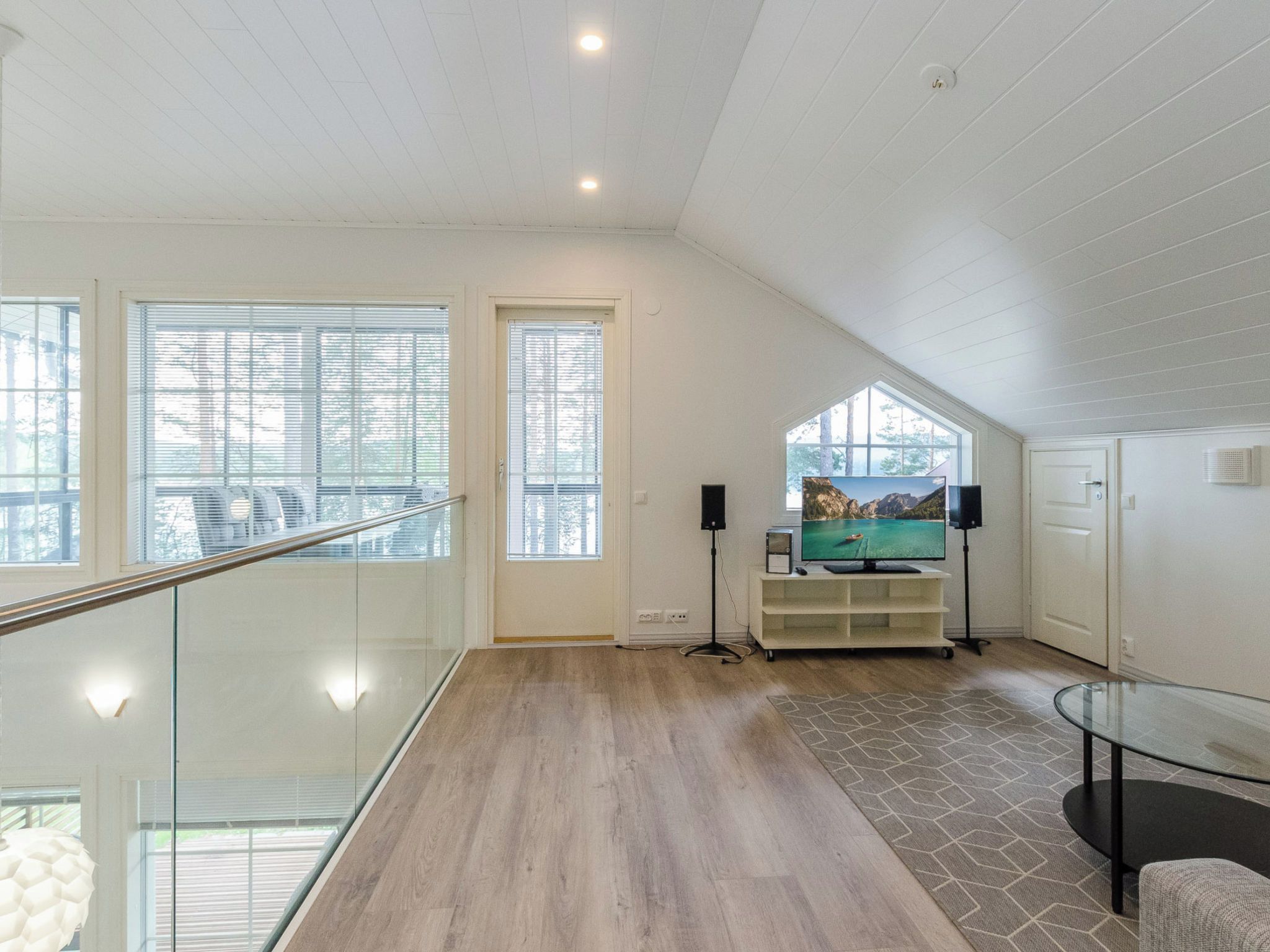 Une pièce spacieuse avec un plancher en bois, une balustrade en verre et une grande fenêtre.