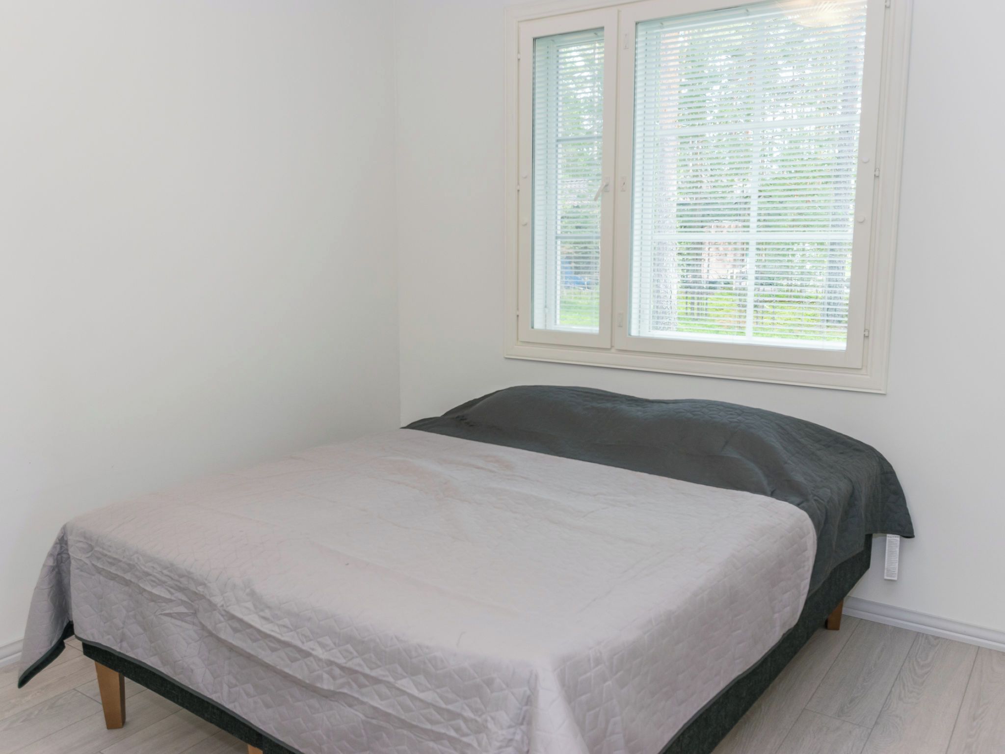 A bedroom with a bed, a window with blinds, and a white wall.