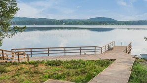Un muelle de madera se adentra en un lago tranquilo, con una colina boscosa al fondo.