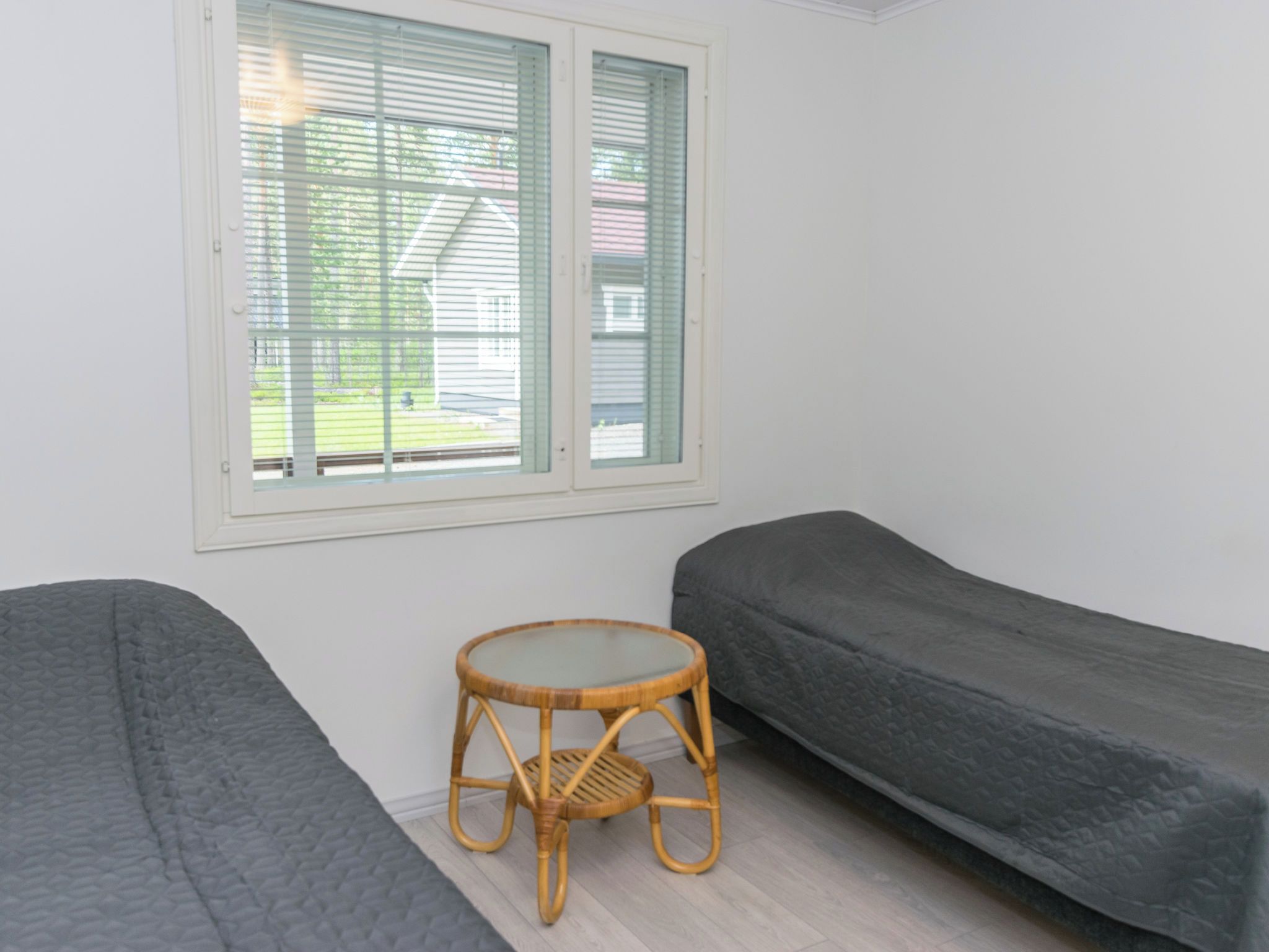 A room with two single beds, a small round table, and a window with blinds.