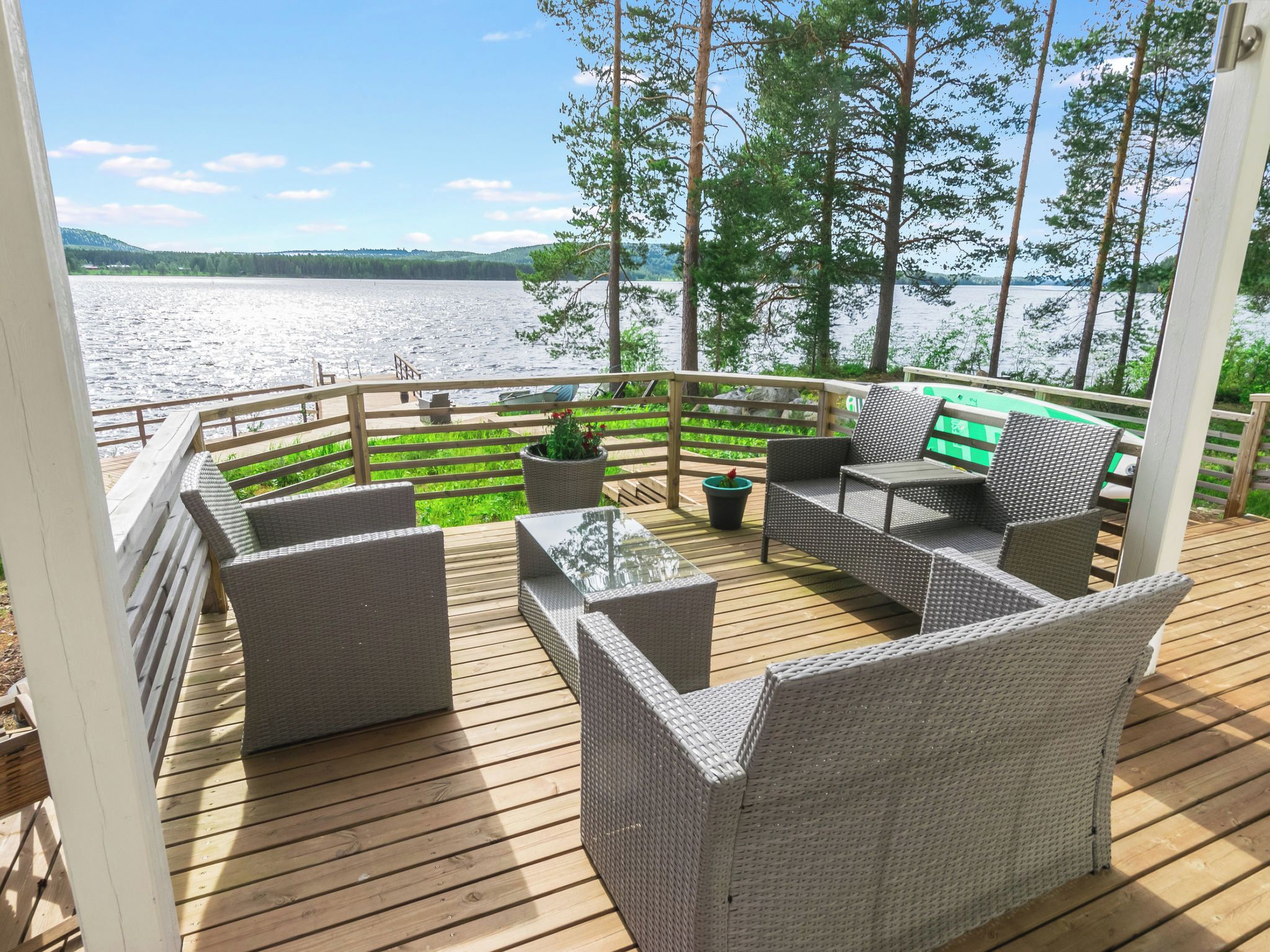 En træterrasse med fletningsmøbler og udsigt til en sø.