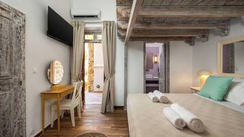 A bedroom with a wooden desk, a bed with rolled towels, a TV, and a bathroom visible through an open door.