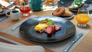 A breakfast setting with a plate of eggs, bacon, and greens, a glass of orange juice, and a croissant on a wooden table. - 4U Rhodes (Rhodes)