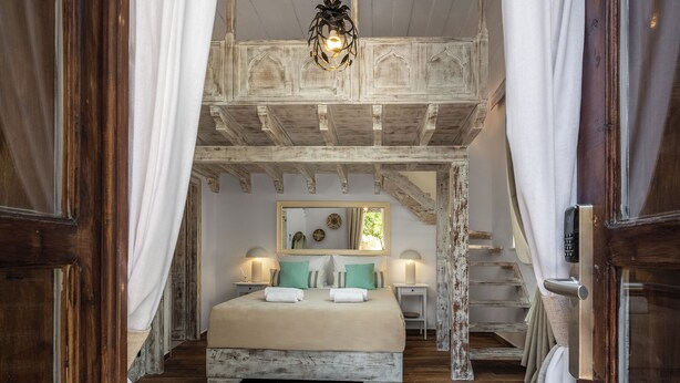 A bedroom with a wooden ceiling, a bed with white bedding, two bedside tables with lamps, and a mirror above the bed. - 4U Rhodes (Rhodes)