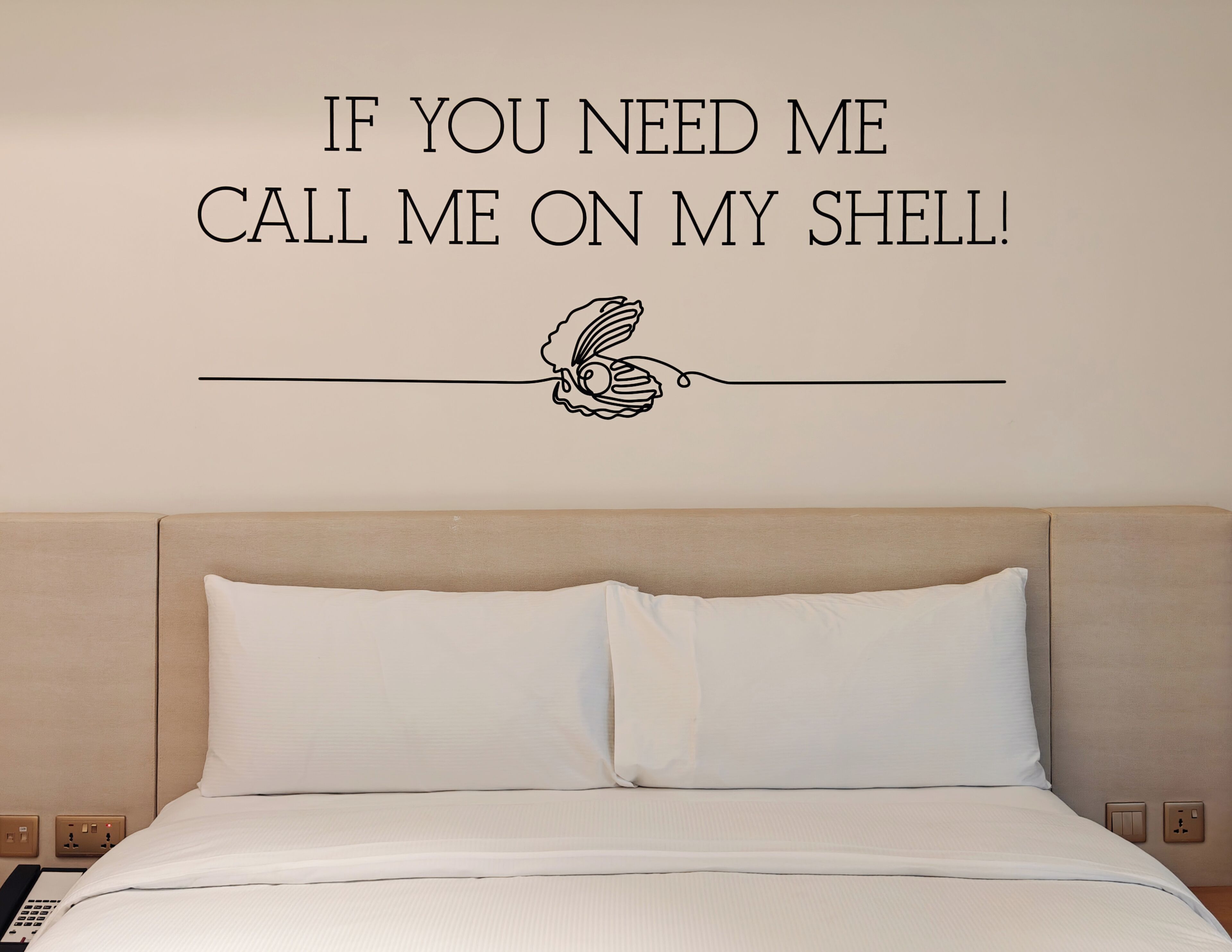 A hotel room with a bed, a wall decal with text, and a power outlet.