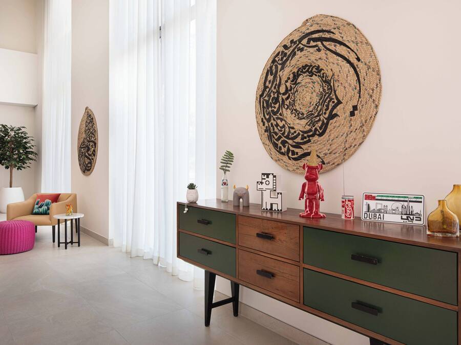 Een moderne woonkamer met een bank, een salontafel, een decoratieve wandversiering en een kast met diverse spullen erop.