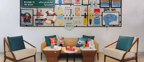 Una sala de estar moderna con un sofá, dos sillones y una mesa de centro. Una obra de arte grande con varios objetos y texto se exhibe sobre el sofá.