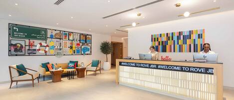 A reception area with a reception desk, two chairs, a sofa, and a wall with various posters and a sign welcoming guests to JBR Beach.