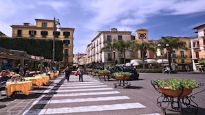 Une rue bordée de terrasses, fréquentée par des piétons et ponctuée d’immeubles à l’architecture classique.