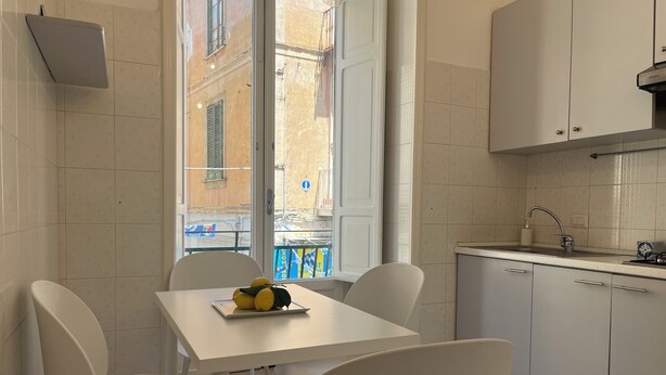 Une cuisine de taille réduite, avec des meubles blancs, un plan de travail blanc et une fenêtre donnant sur la rue.