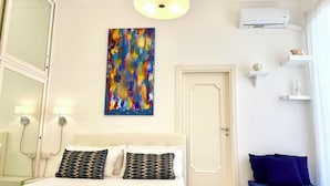 Une chambre d’hôtel comprenant un lit, des lampes de chevet, un climatiseur fixé au mur, une porte et une étagère ornée d’objets décoratifs.